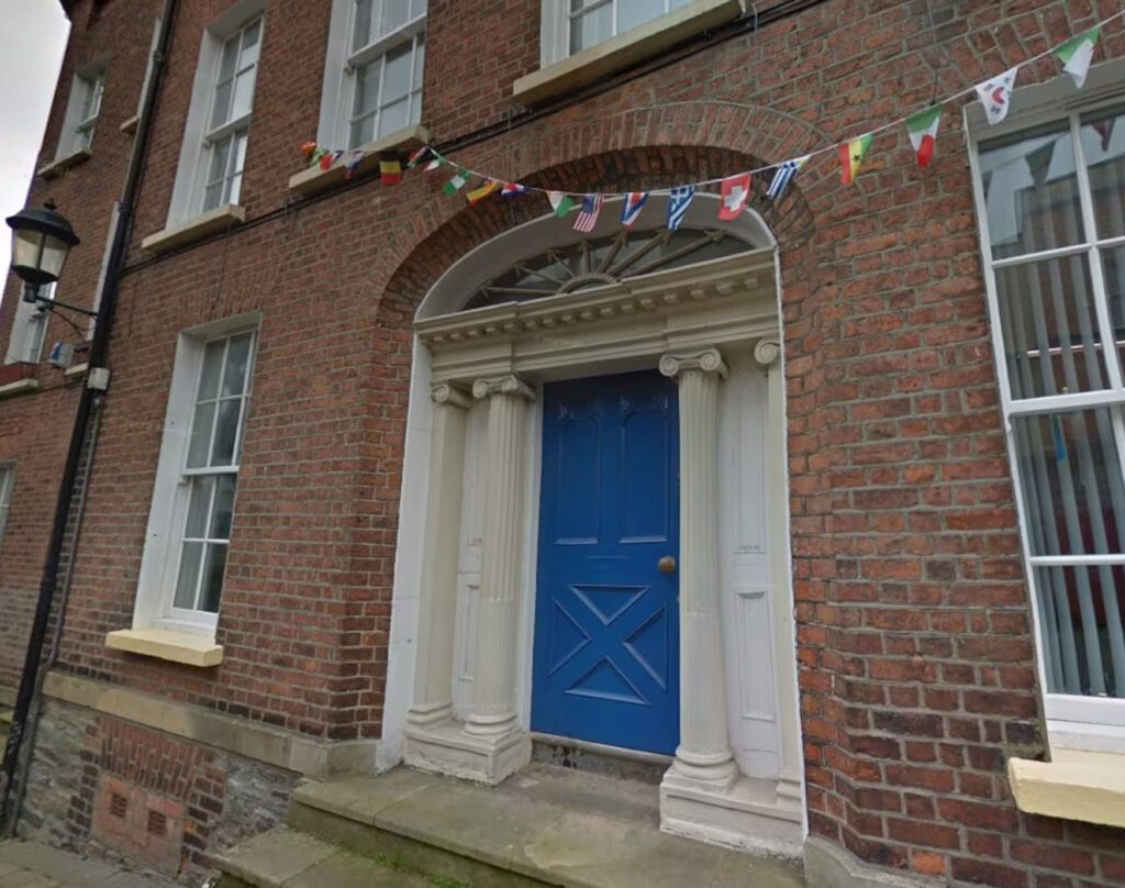 A blue door with a decorative frame on a brick building in Derry, featuring student accommodation vibes and a small flag bunting above, reminiscent of Magazine St. charm.
