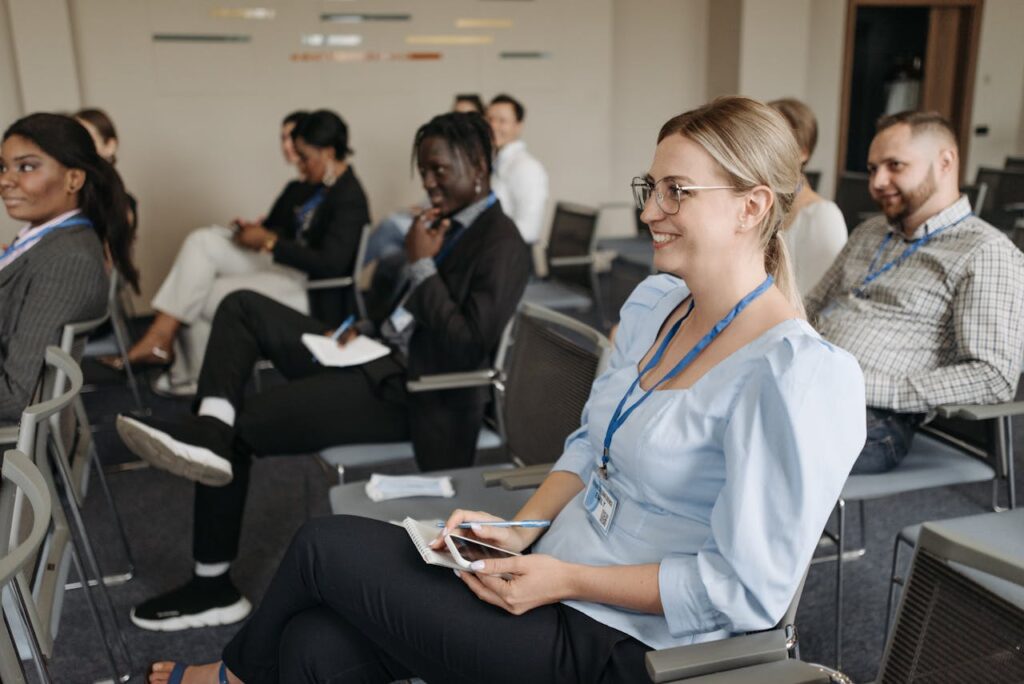 A group of people sits in a conference room, some smiling, with notepads and phones in hand, wearing name tags on blue lanyards. They're engaged in a discussion focused on fire safety and risk assessment strategies.