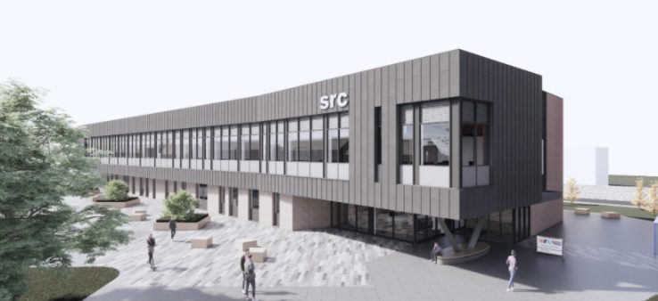 A modern two-story building with large windows and the letters "SRC" on the facade; people walk and sit in the surrounding paved outdoor area.