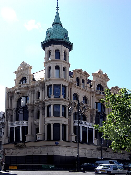 Three-story corner building in Derry/Londonderry with ornate architecture, a central tower topped by a green dome, large arched windows, and parked cars along the street—home to the iconic Austin's.